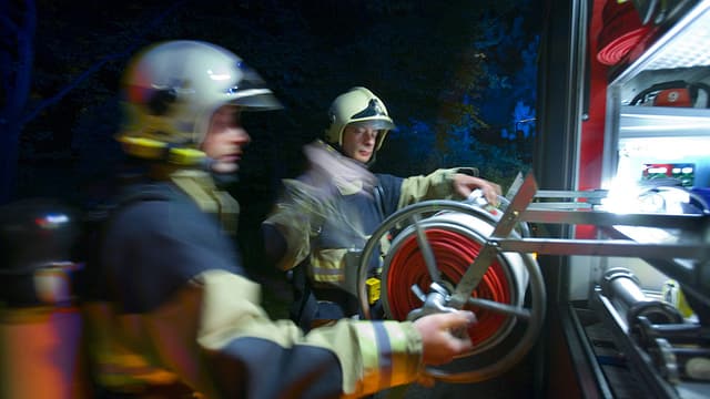 Zwei Feuerwehrmänner nehmen den Schlauch vom Wagen. Zwei Feuerwehrmänner nehmen den Schlauch vom Wagen.