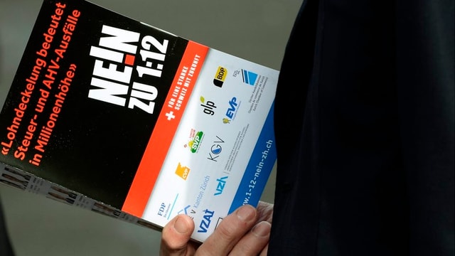 Hier ist eine Hand zu sehen, die einen Prospekt «Nein zu 1:12» hält. Hier ist eine Hand zu sehen, die einen Prospekt «Nein zu 1:12» hält.