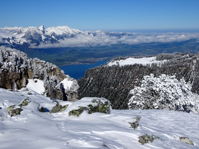 Im Vordergrund Neuschnee, weit unten der Thunersee und im Hintergrund das Mitteland.