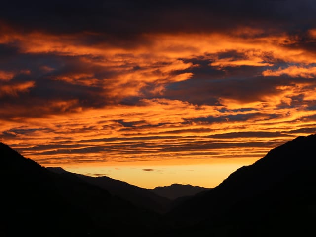 Ktischig organger Himmel über einem Tal.