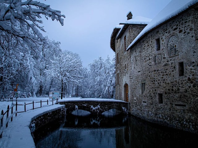 Schloss mit Wassergraben bei Schnee und Wolkendecke