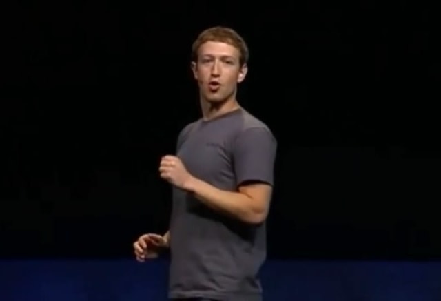 Ein Mann in grauem T-Shirt vor dunkelblauem Hintergrund, er spricht.