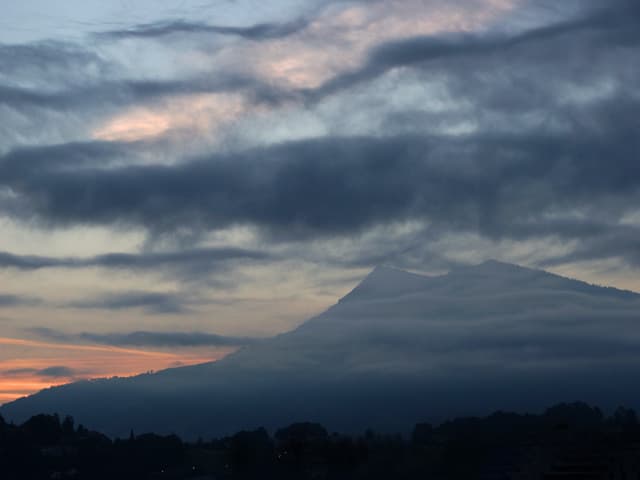 Die Rigi umgeben von grauen Nebelfeldern und dunklen Wolken. Im Hintergrund schwaches Morgenrot.