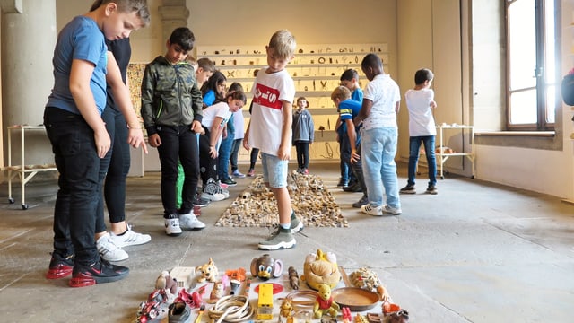 Kunstinstallation aus Abfällen, die am Boden liegen. Kinder betrachten intensiv die gesammelten Dinge. Kunstinstallation aus Abfällen, die am Boden liegen. Kinder betrachten intensiv die gesammelten Dinge.