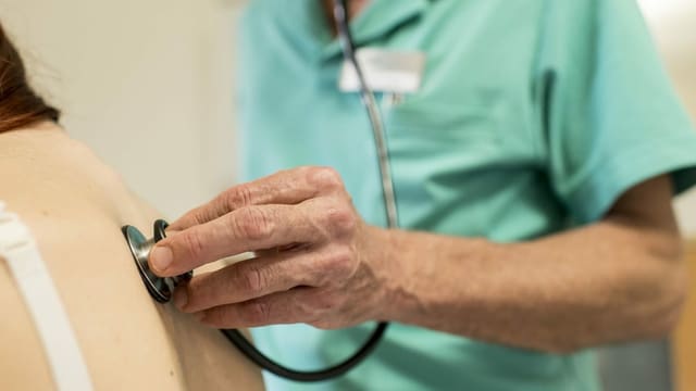 Ein Arzt hört mit einem Stethoskop den Rücken einer Patientin ab Ein Arzt hört mit einem Stethoskop den Rücken einer Patientin ab