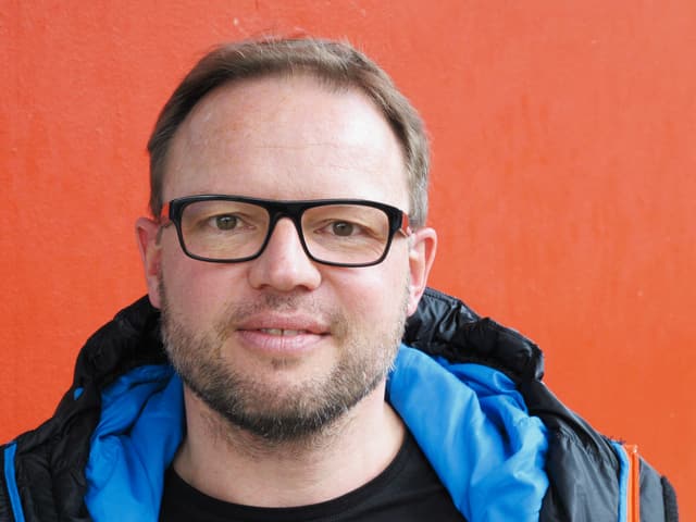 Mann mit blauer Kapuze und Brille vor rotem Hintergrund. Mann mit blauer Kapuze und Brille vor rotem Hintergrund.