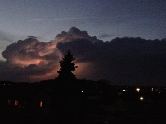 Am Horizont leuchtet eine Gewitterwolke orange auf. In der Abenddämmerung ist der Himmel über den Wolken noch bläulich.
