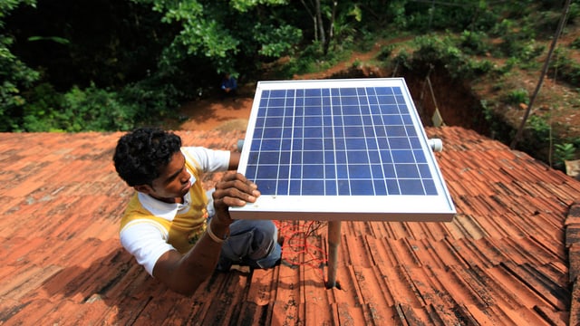 Ein Mann montiert ein Solarpanel auf ein Dach Ein Mann montiert ein Solarpanel auf ein Dach