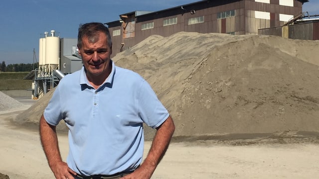 Mann vor Sandhaufen und Werksgebäude. Mann vor Sandhaufen und Werksgebäude.