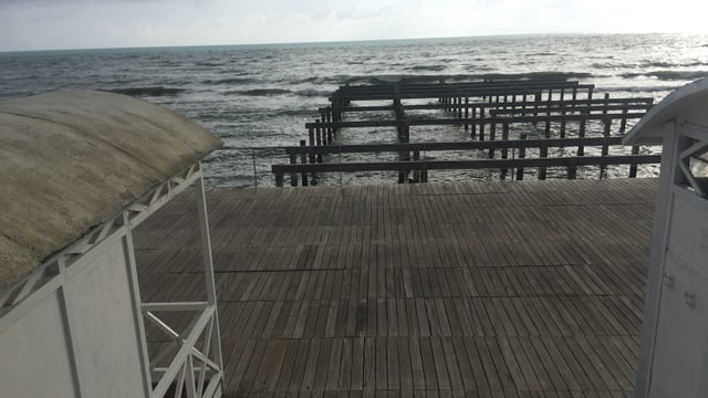 Im Vordergrund die Strandhäuschen auf einer mit Holz bedeckten Plattform, dahinter aus dem Meer ragende Holzpfähle. Im Vordergrund die Strandhäuschen auf einer mit Holz bedeckten Plattform, dahinter aus dem Meer ragende Holzpfähle.