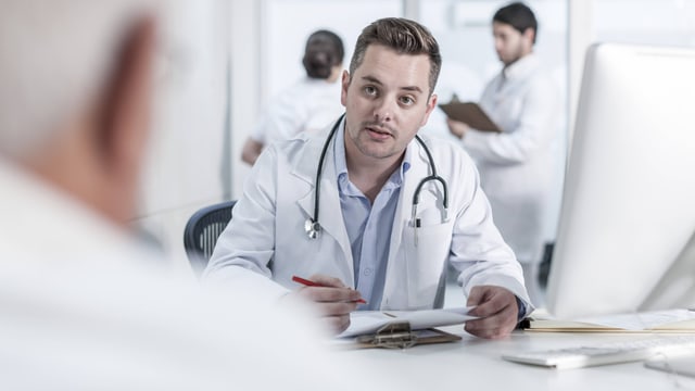 Arzt und Patient sitzen sich an einem Tisch gegenüber. Arzt und Patient sitzen sich an einem Tisch gegenüber.