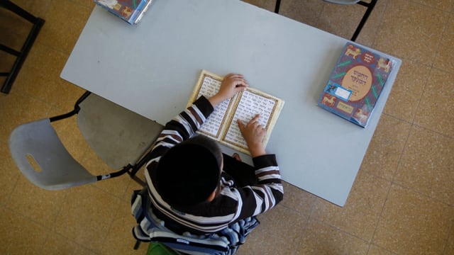 Ein jüdischer Schüler mit einer Kippa sitzt in der Schulbank. Ein jüdischer Schüler mit einer Kippa sitzt in der Schulbank.
