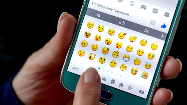 Eine Hand tippt Emojis auf einem Smartphone-Display. Eine Hand tippt Emojis auf einem Smartphone-Display.