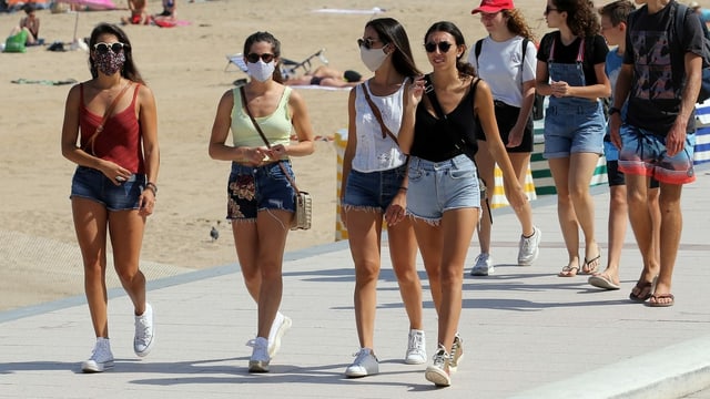 Junge Leute mit und ohne Masken laufen am Strand.