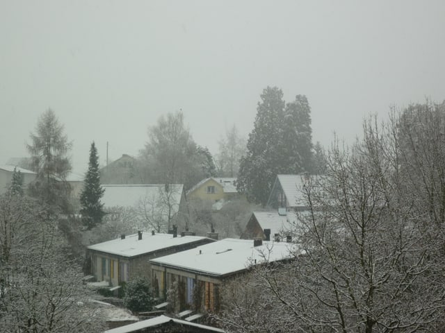 Hausdächer und Bäume sind mit etwas Schnee bedeckt.