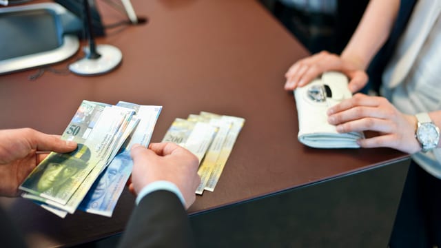 Eine Hand zahlt an einem Bankschalter Geld aus. Eine Hand zahlt an einem Bankschalter Geld aus.