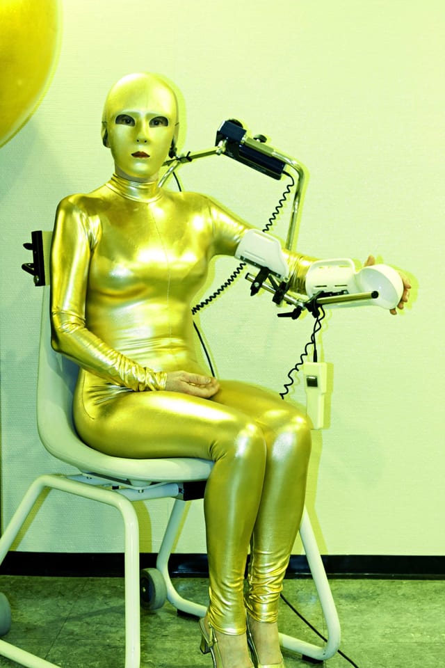 Eine Frau sitzt im goldenen Latex-Overall auf einem Stuhl. Eine Frau sitzt im goldenen Latex-Overall auf einem Stuhl.