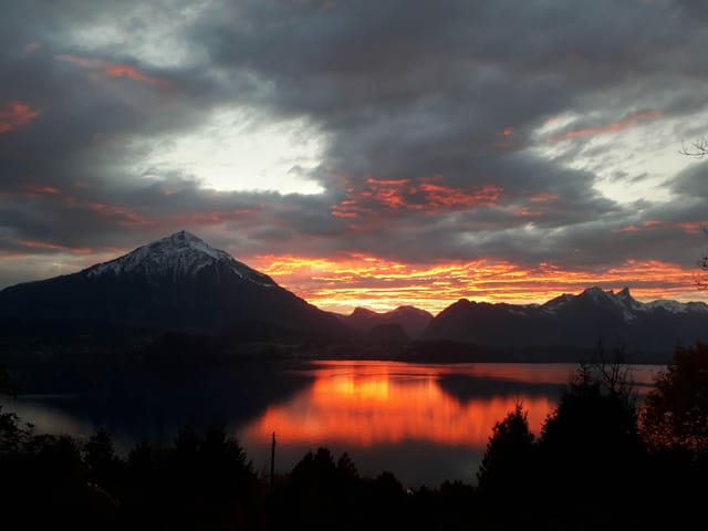 Merligen/BE: Abendstimmung mit Blick auf den Niesen. Der Himmel hat sich orange-rot verfärbt. Davor sieht man schwarz den Thunersee.