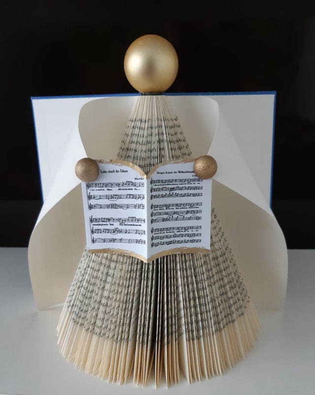 Gefalteter Engel mit Musiknoten in der Hand.