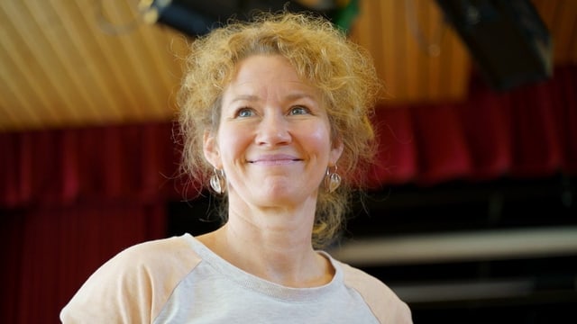 Eine Frau mit blonden langen Locken lächelt an der Kamera vorbei. Eine Frau mit blonden langen Locken lächelt an der Kamera vorbei.