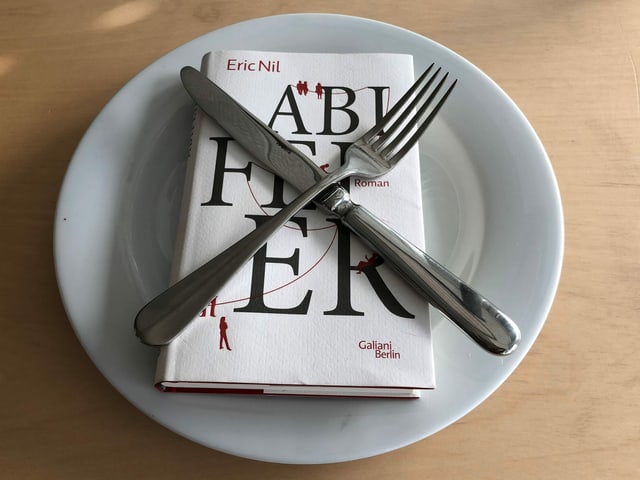«Abifeier» von Eric Nil liegt auf einem weissen Teller. Messer und Gabel in 20-nach-8-Stellung darüber. 