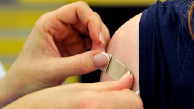 Hände kleben ein Pflaster auf eine Schulter. Hände kleben ein Pflaster auf eine Schulter.