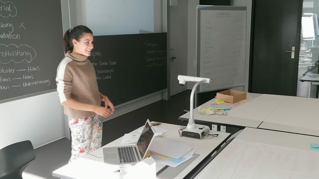 Junge Frau vor Wandtafel und Computer erklärt etwas Junge Frau vor Wandtafel und Computer erklärt etwas