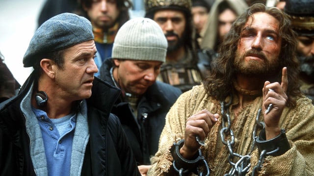 Ein Mann mit Kappe sitzt neben einem Mann, der als Jesus verkleidet ist. Ein Mann mit Kappe sitzt neben einem Mann, der als Jesus verkleidet ist.