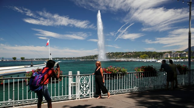 Ein Mann fotografiert eine Frau, sie steht am Genferseeufer mit dem Jet d'eau im Hintergrund. Ein Mann fotografiert eine Frau, sie steht am Genferseeufer mit dem Jet d'eau im Hintergrund.