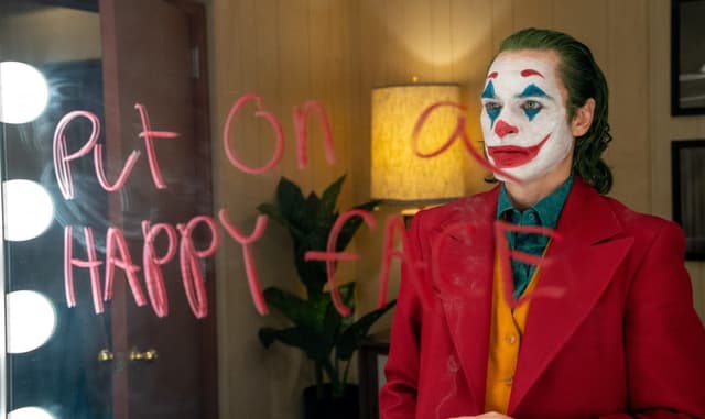 Ein Mann in rotem Anzug steht vor einem Spiegel, auf dem rot geschrieben steht: «Put on a happy face». Ein Mann in rotem Anzug steht vor einem Spiegel, auf dem rot geschrieben steht: «Put on a happy face».