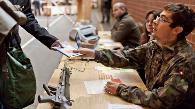 Ein Soldat der Schweizer Armee gibt sein Sturmgewehr ab und erhält sein Dienstbüchlein zurück. Ein Soldat der Schweizer Armee gibt sein Sturmgewehr ab und erhält sein Dienstbüchlein zurück.