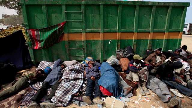 Flüchtlinge und Migranten liegen in einer Reihe an einer Mülltonne. Flüchtlinge und Migranten liegen in einer Reihe an einer Mülltonne.