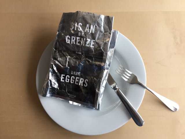Das zerknüllte Cover von Dave Eggers neuem Roman «Bis an die Grenze» auf weissem Teller Das zerknüllte Cover von Dave Eggers neuem Roman «Bis an die Grenze» auf weissem Teller