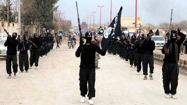 Personen in Schwarz mit schwarzen IS-Flaggen marschieren durch eine Strasse. Personen in Schwarz mit schwarzen IS-Flaggen marschieren durch eine Strasse.