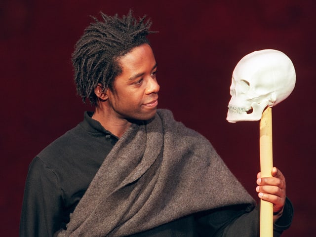Adrian Lester hält einen Holzstab mit weissem Totenschädel Adrian Lester hält einen Holzstab mit weissem Totenschädel