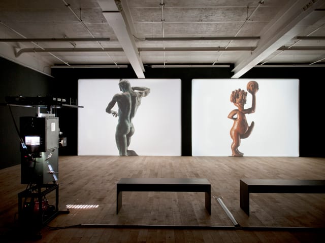 Usstellungsraum mit zwei Leinwänden nebneinander, auf denen die zwei Statuen von Prometheus und einer Zwitterfigur zu sehen sind. Usstellungsraum mit zwei Leinwänden nebneinander, auf denen die zwei Statuen von Prometheus und einer Zwitterfigur zu sehen sind.
