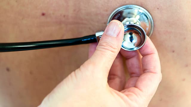 Nahaufnahme einer Hand, die ein Stetoskop an den Rücken eines Patienten drückt. Nahaufnahme einer Hand, die ein Stetoskop an den Rücken eines Patienten drückt.