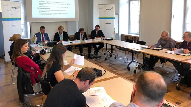 Pressekonferenz. Journalisten sitzen links und rechts an Tischen und schreiben. Vorne reden Leute. Pressekonferenz. Journalisten sitzen links und rechts an Tischen und schreiben. Vorne reden Leute.
