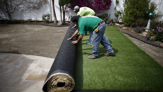Arbeiter rollen Kunstrasen im Garten aus Arbeiter rollen Kunstrasen im Garten aus