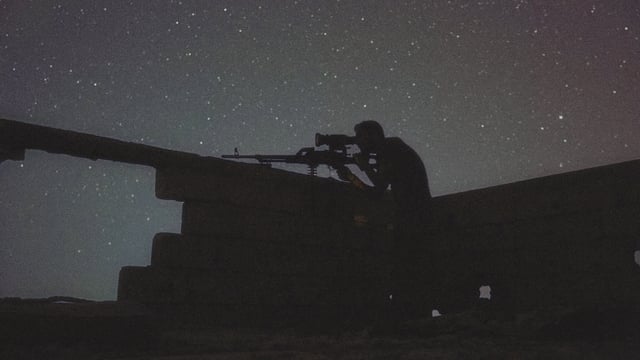 Eine Aufnahme im Dunkeln von einem Mann, der in einer Festung steht und eine Waffe hält. Eine Aufnahme im Dunkeln von einem Mann, der in einer Festung steht und eine Waffe hält.
