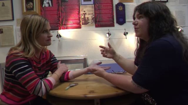 Zwei Frauen an einem Tisch, die eine liest die Hand der anderen Zwei Frauen an einem Tisch, die eine liest die Hand der anderen