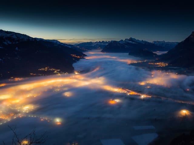 Im Tal liegt Nebel, die Lichter scheinen hindurch.
