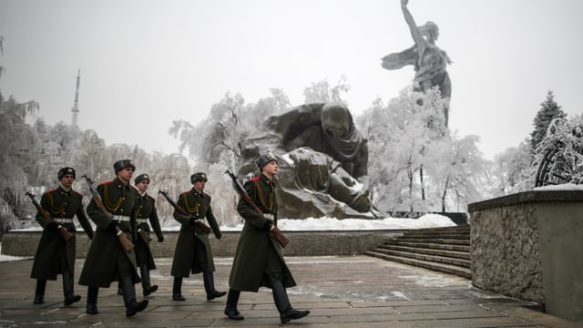 Sicherheitskräfte marschieren an einer Statue in Wolgograd vorbei. Sie tragen lange Mäntel und Stiefel. Sicherheitskräfte marschieren an einer Statue in Wolgograd vorbei. Sie tragen lange Mäntel und Stiefel.
