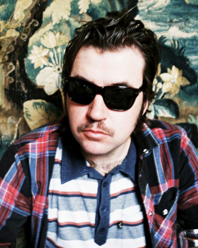 Albert Serra mit Sonnenbrille vor einem bunten Gemälde. Albert Serra mit Sonnenbrille vor einem bunten Gemälde.