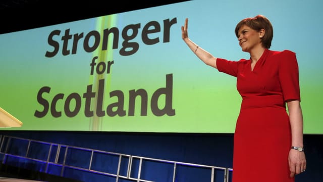 Eine Frau in einem roten Kleid winkt vor einem Plakat mit der Aufschrift «Stronger for Scotland». Eine Frau in einem roten Kleid winkt vor einem Plakat mit der Aufschrift «Stronger for Scotland».