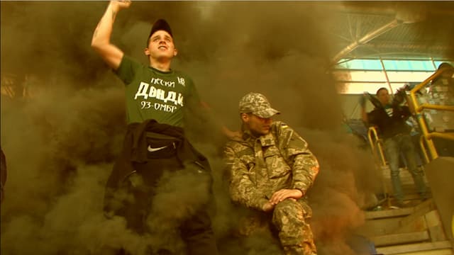 Ein Fan und ein Mann in Kampfmontur inmitten von Rauchschwaden in einem Stadion. Ein Fan und ein Mann in Kampfmontur inmitten von Rauchschwaden in einem Stadion.