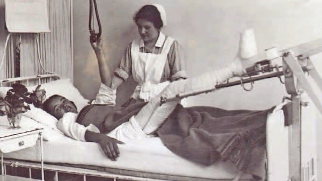 Eine alte Schwarzweiss-Aufnahme zeigt eine Krankenpflegerin am Bett einer Patientin, die einen Fuss eingegipst hat und sich von der Krankenpflegerin versorgen lässt. Eine alte Schwarzweiss-Aufnahme zeigt eine Krankenpflegerin am Bett einer Patientin, die einen Fuss eingegipst hat und sich von der Krankenpflegerin versorgen lässt.