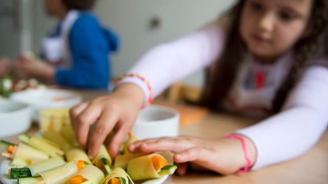 Ein Kind richtet einen Teller mit Gemüse an.