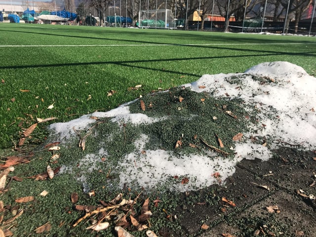 Schneehaufen an einem Spielfeldrand, voll grünem Granulat