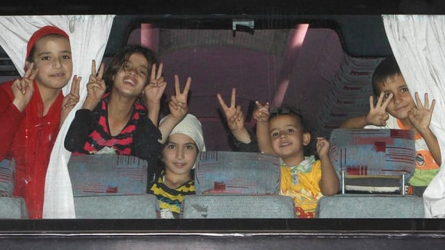 Kinder machen in einem Busfenster Siegeszeichen. Kinder machen in einem Busfenster Siegeszeichen.